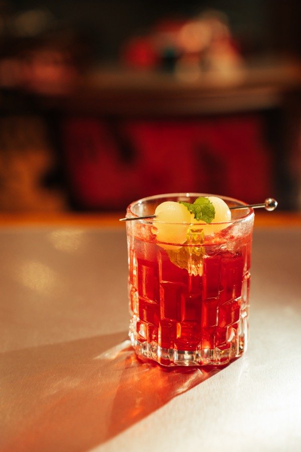 Minuman merah cerah dengan hiasan leci di The Social Solitude