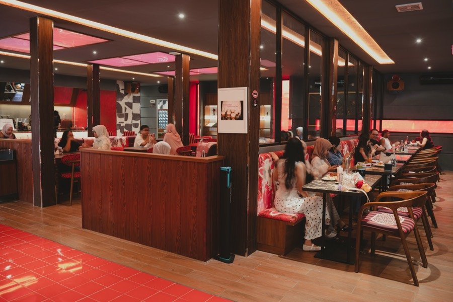 Tamu bersantap di interior The Social Solitude yang hangat dengan nuansa merah dan kayu